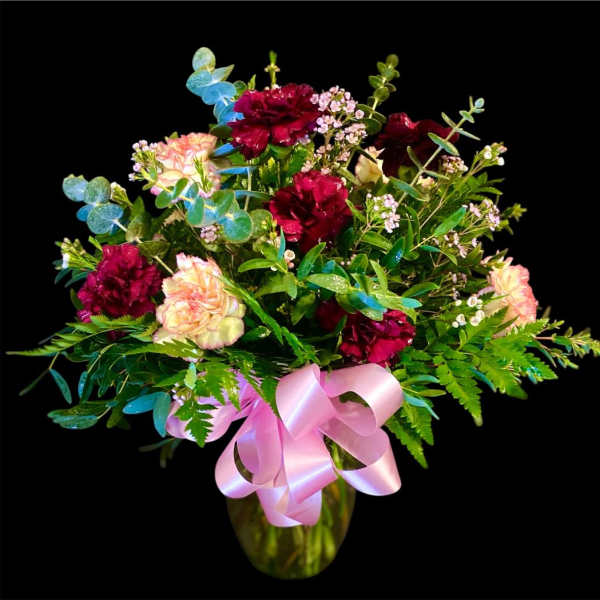 Bouquet of burgundy and blush carnations in a glass vase with a pink ribbon