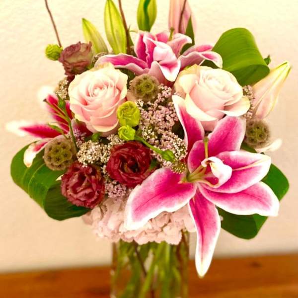 Pink lilies and roses arranged in a clear glass vase