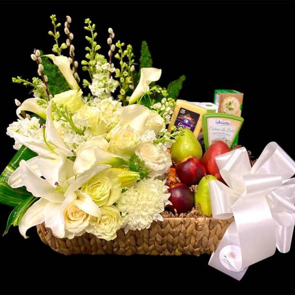 White floral arrangement in a woven basket with fruit and cheese boxes