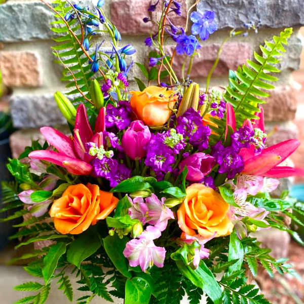 Colorful bouquet of orange roses, pink lilies, and purple flowers in a vase