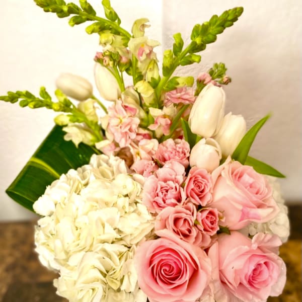 Pink roses and white hydrangeas in a low vase with tulips and snapdragons