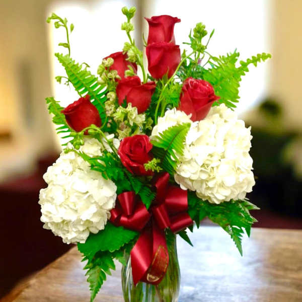 Red roses and white hydrangeas in a glass vase with a red ribbon
