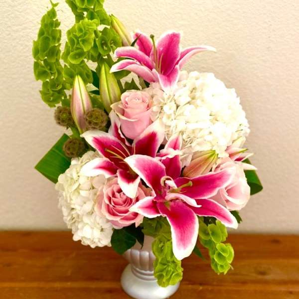 Pink lilies and roses arranged with white hydrangeas in a white vase