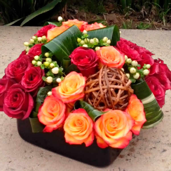 Red and orange roses arranged in a low black container with woven accents
