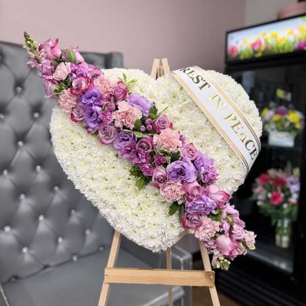Heart-shaped floral tribute with pink and purple flowers on an easel