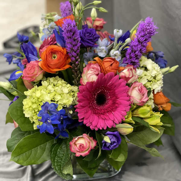 Colorful mixed bouquet with gerbera daisies, roses, and hydrangeas in a glass vase
