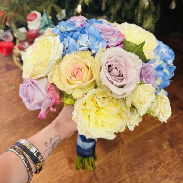 Handheld bouquet of pastel roses and blue hydrangeas