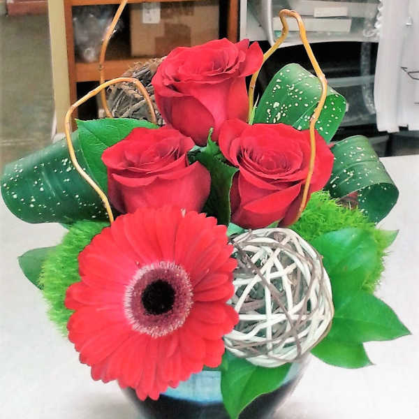 Red roses and a gerbera daisy in a decorative basket arrangement