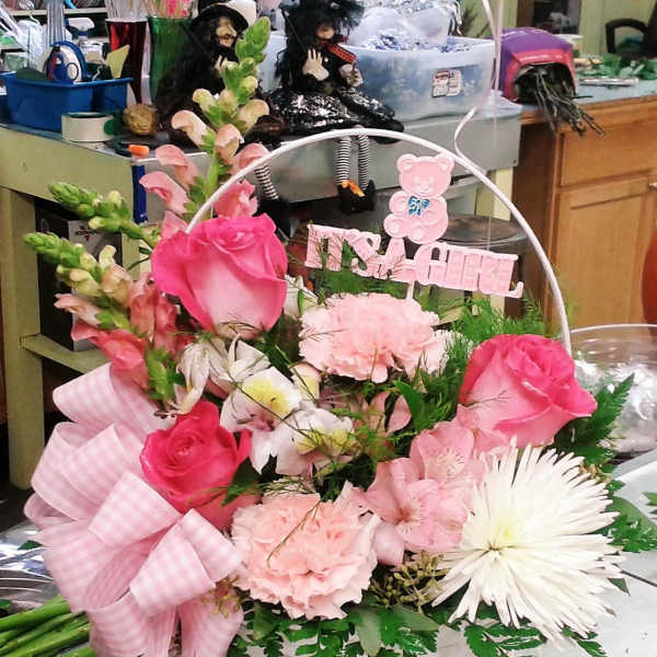 Pink and white flower basket with a ribbon and "It's a Girl" sign