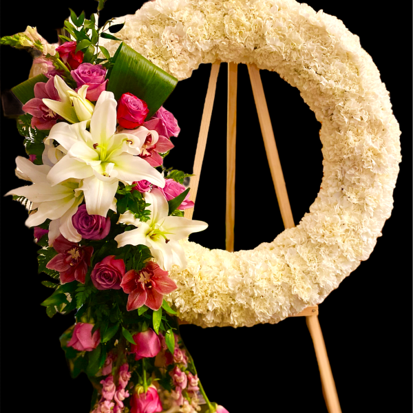 Floral wreath on an easel beside a cascading bouquet of lilies and roses