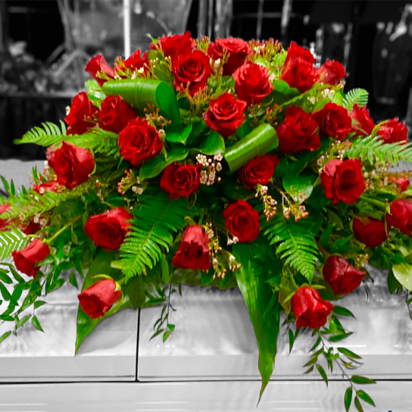 Large arrangement of red roses with green foliage on a white casket