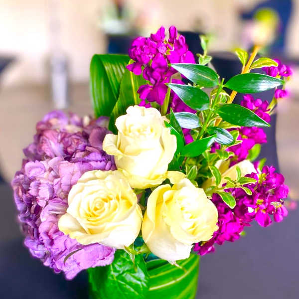 Cream roses and purple flowers arranged in a green glass vase