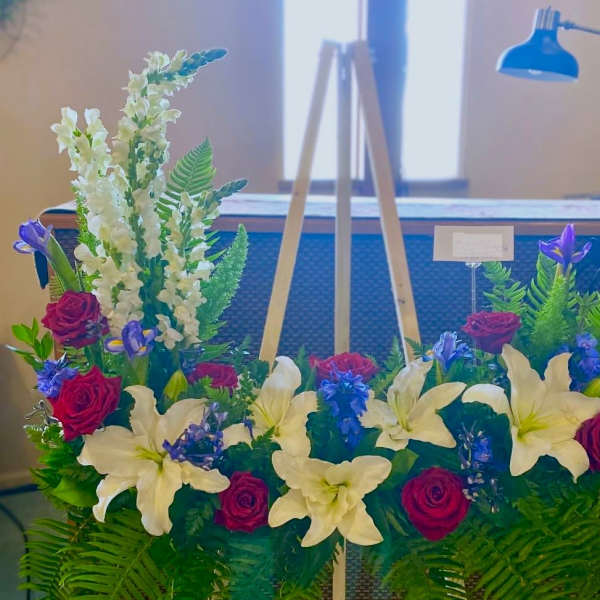 Floral arrangement with white lilies, red roses, and purple blooms on an easel