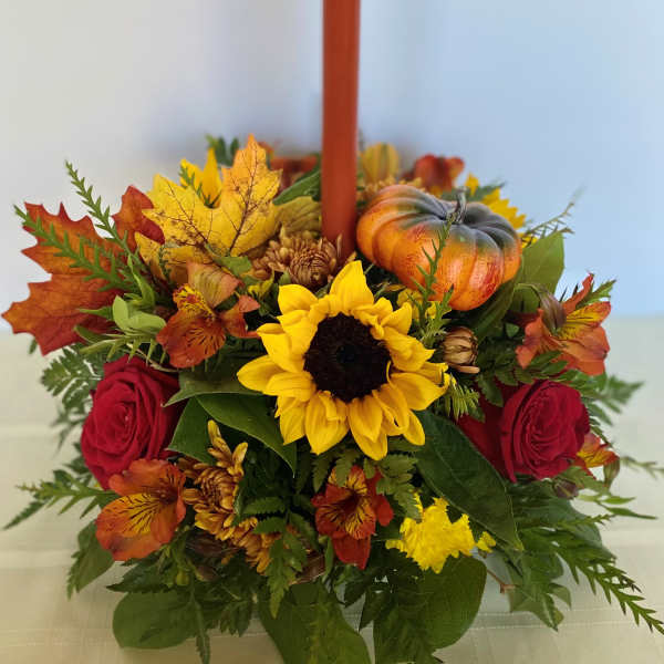 Autumn floral centerpiece with a red candle, sunflower, roses, and a small pumpkin