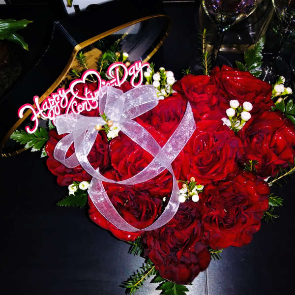Heart-shaped bouquet of red roses with a pink ribbon and "Happy Anniversary" topper