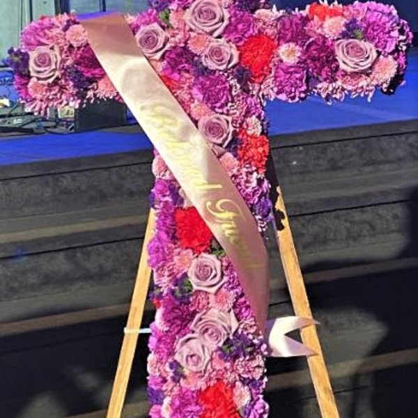Cross-shaped floral tribute with pink and purple flowers on an easel