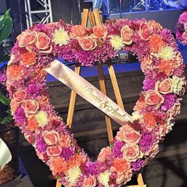 Heart-shaped floral wreath with pink roses and purple flowers on an easel