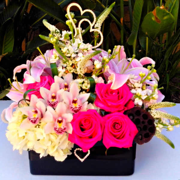Pink roses and lilies arranged in a black box with heart picks