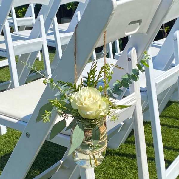 White rose in a small hanging glass vase on a chair