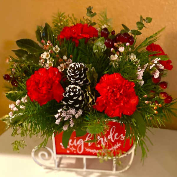 Red carnations arranged with pinecones and greenery in a holiday container