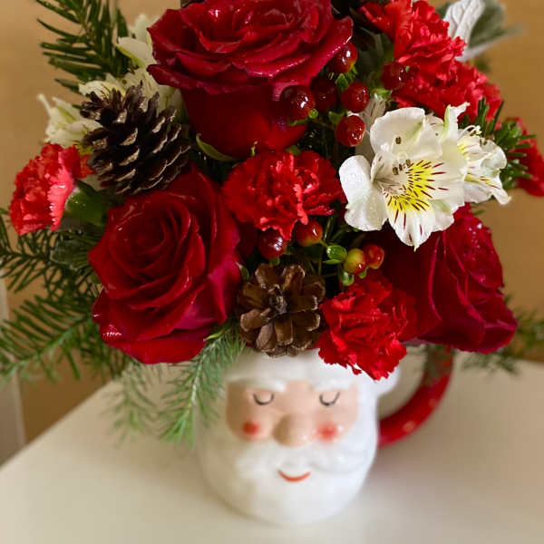 Red roses and carnations arranged in a Santa mug with pinecones.