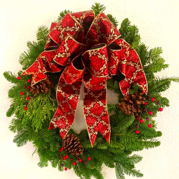 Christmas wreath with a red patterned bow, pinecones, and evergreen branches