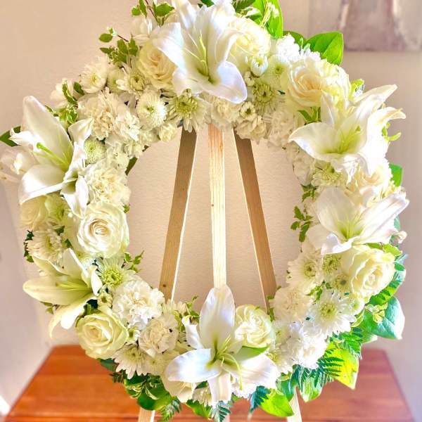 White floral wreath with lilies and roses on a wooden easel