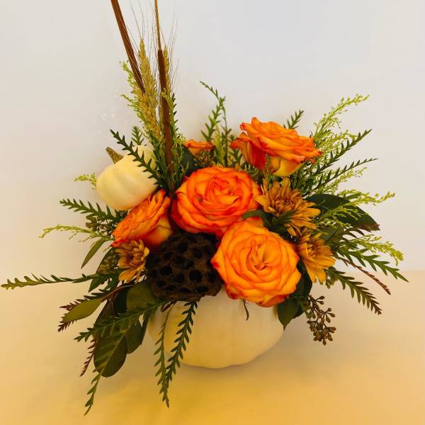 Orange roses arranged in a white pumpkin container with dried wheat accents