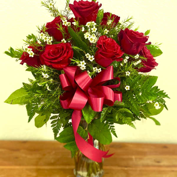 Red roses arranged in a clear glass vase with a pink ribbon