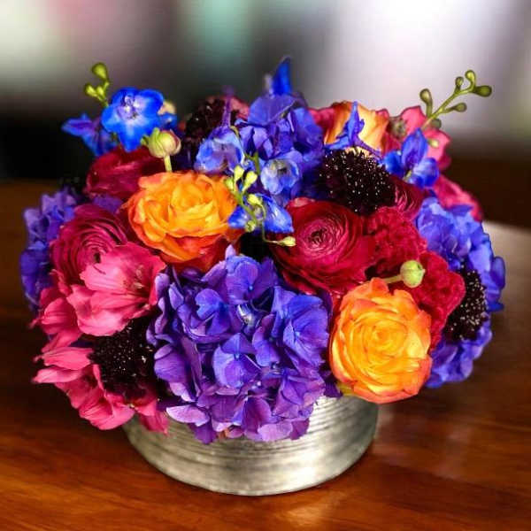 Bright mixed bouquet in a low silver vase with purple, pink, and orange blooms