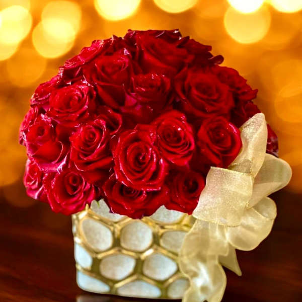 Red rose bouquet in a gold-and-white vase with a cream ribbon