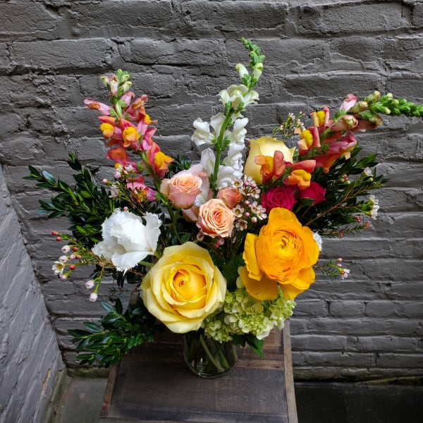 Mixed bouquet of roses, ranunculus, and snapdragons in a glass vase