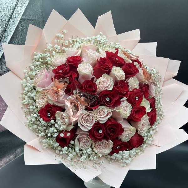 Round bouquet of red and blush roses with baby's breath in pink wrapping paper.