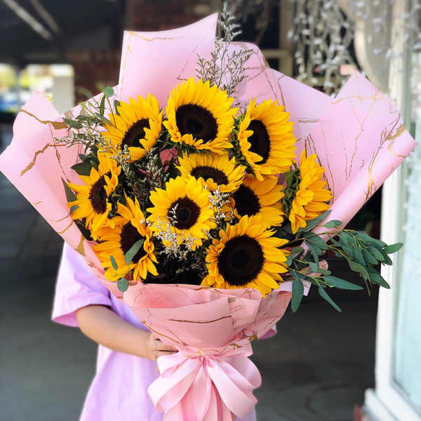 Large bouquet of sunflowers wrapped in pink paper with a ribbon