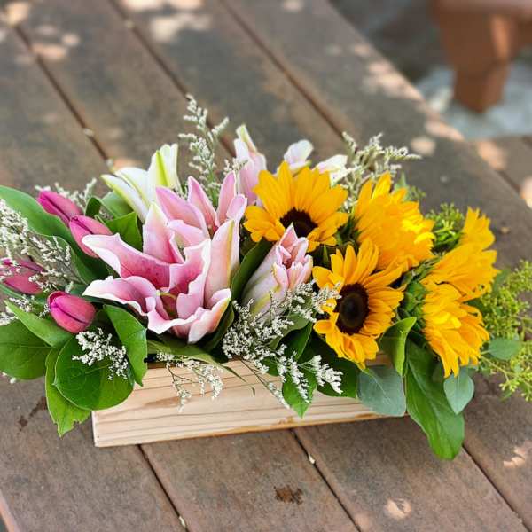 Pink lilies and yellow sunflowers in a wooden box