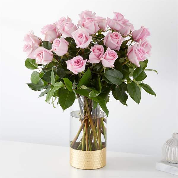 Pink roses arranged in a clear glass vase with a gold base