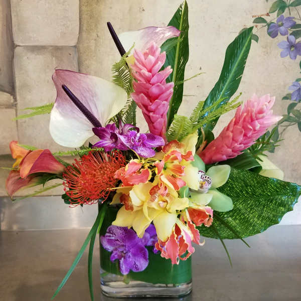 Tropical flower arrangement with orchids, calla lilies, and pink ginger in a glass vase
