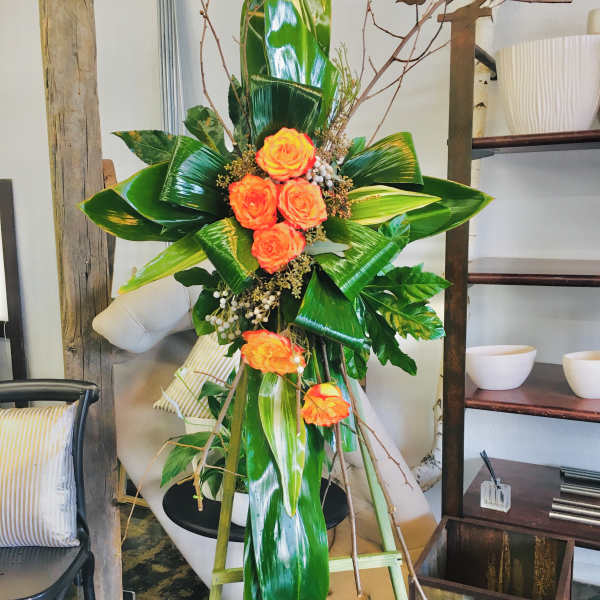 Tall floral standing arrangement with orange roses and glossy tropical leaves
