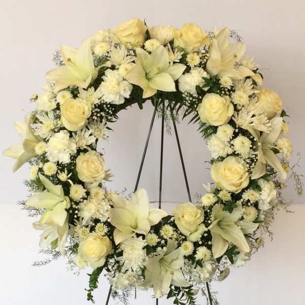 Cream floral wreath on a black stand with roses and lilies