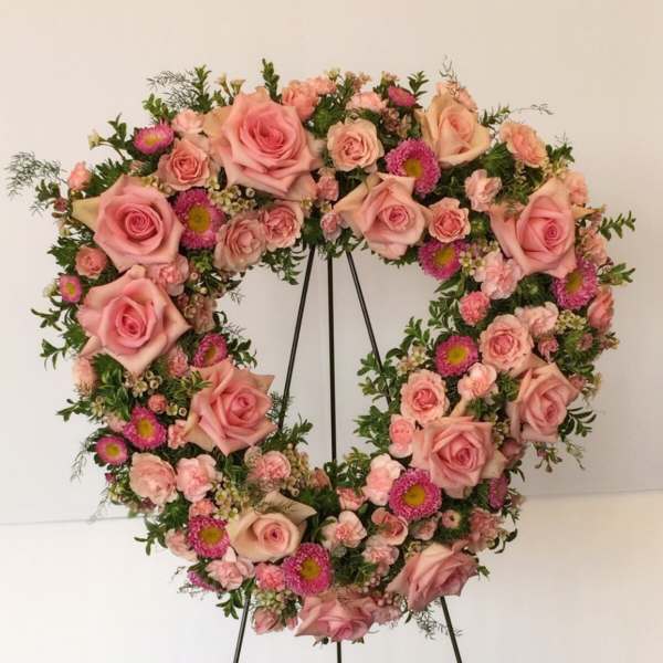 Heart-shaped floral wreath of pink roses and small pink blooms on a stand