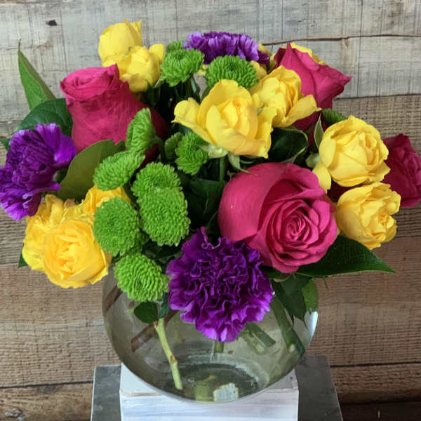 Bouquet of pink and yellow roses with purple and green pom-pom flowers in a glass vase