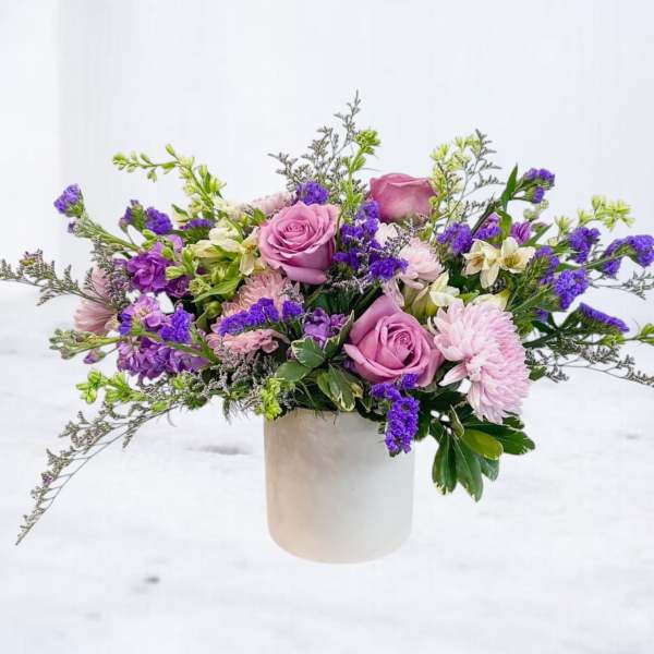 Lavender roses and purple flowers in a white cylindrical vase