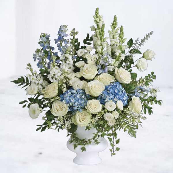Tall white and blue arrangement with roses and hydrangeas in a white pedestal vase