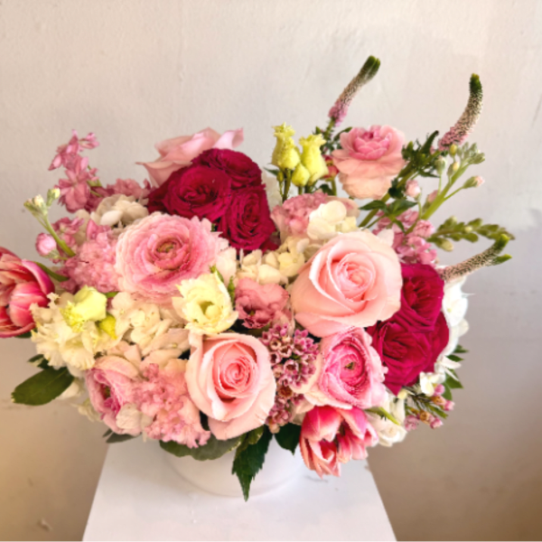 Low pink and white flower arrangement with roses, ranunculus, tulips, and hydrangeas in a white bowl vase