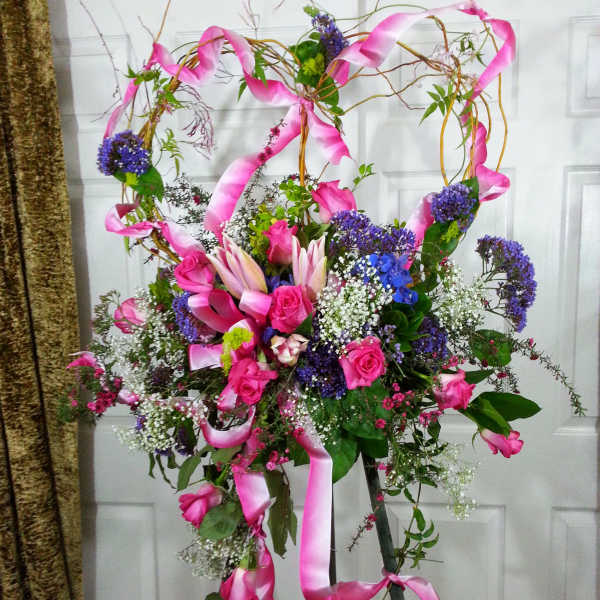 Tall floral spray with pink roses, lilies, and purple accents on a stand
