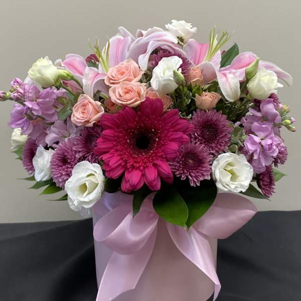 Pink and white mixed flower arrangement in a round pink box with ribbon