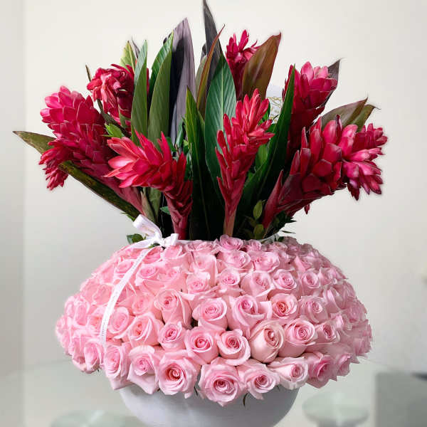 Pink roses in a white bowl with red tropical flowers above