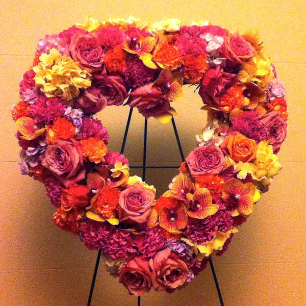 Heart-shaped floral wreath with pink, red, and yellow blooms on a stand