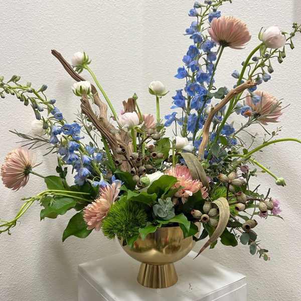 Mixed floral arrangement in a gold vase with blue and blush blooms