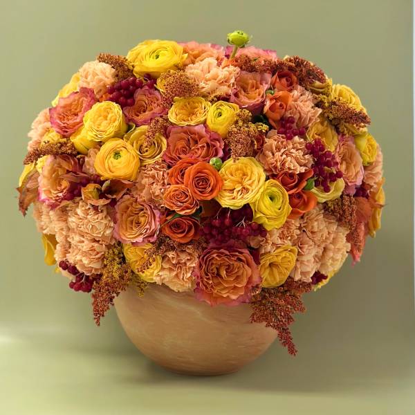 Round bouquet of yellow, peach, and orange flowers in a vase